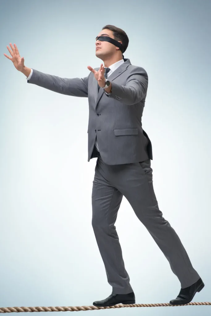 A blindfolded man in a suit walking on a tightrope, symbolizing uncertainty or fear about dental extraction affecting vision.
