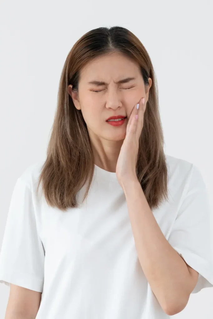 Woman touching her cheek with a pained expression, showing discomfort after a tooth extraction and the challenges of post-removal recovery.